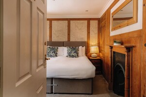 Un dormitorio con cama, mesita de noche, espejo y chimenea.