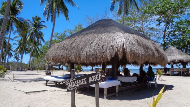 Un espace de massage aménagé sur la plage, doté de parasols en chaume et de chaises longues.