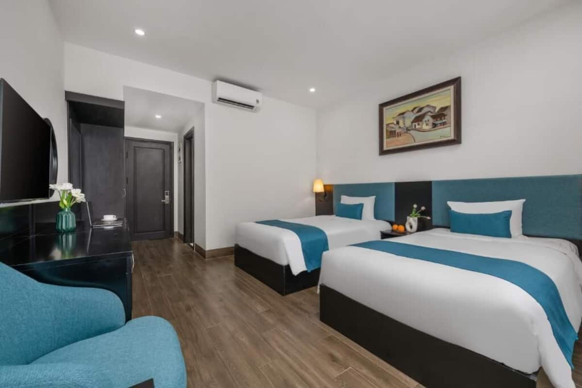 A hotel room with two beds, a TV, a desk, and a painting on the wall.