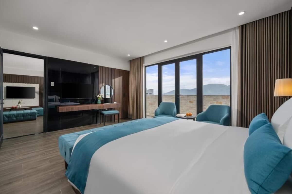 A hotel room with a large bed, a desk, a TV, and a view of the mountains.