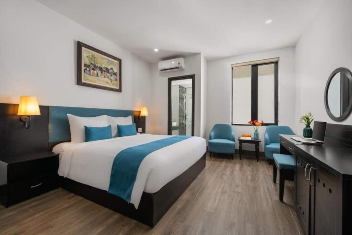 A modern hotel room with a large bed, two bedside lamps, a desk, and a chair.