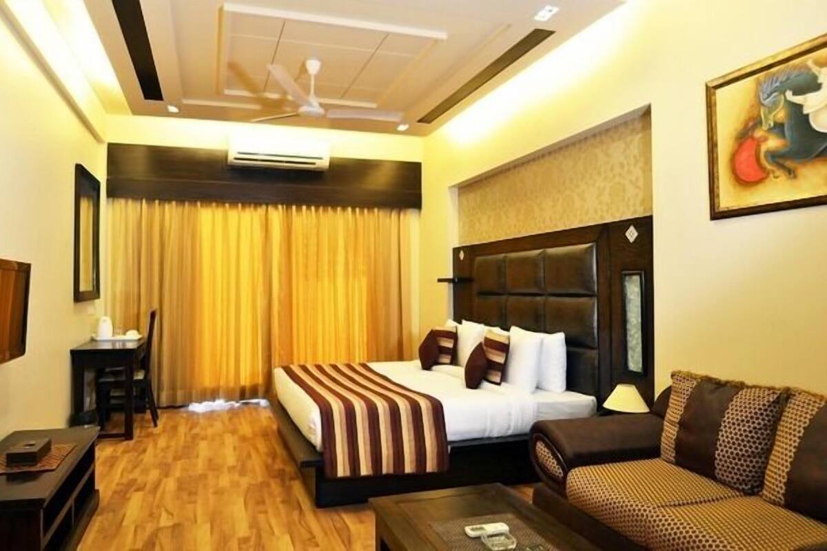 A hotel room with a bed, a sofa, a desk, and an air conditioning unit.