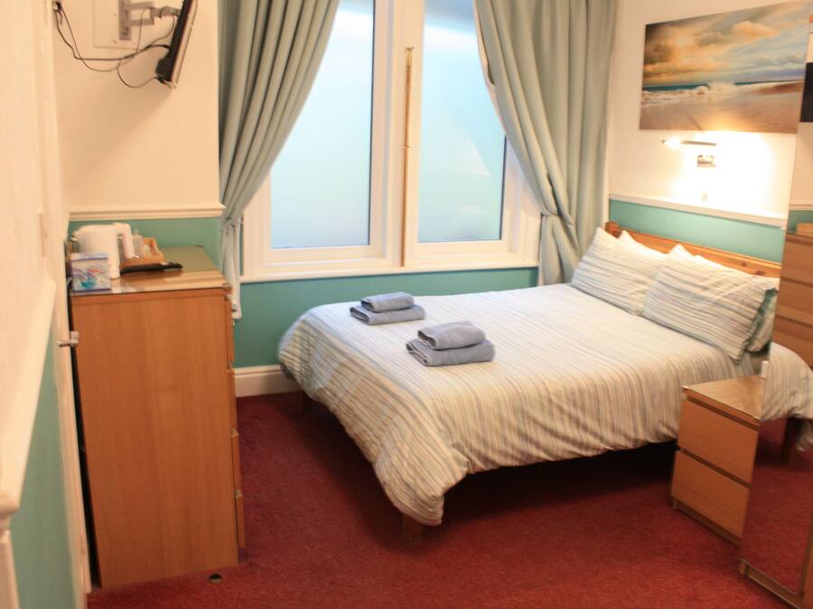 Une chambre à coucher comprenant un lit, une table de chevet, une commode et une fenêtre avec des rideaux.