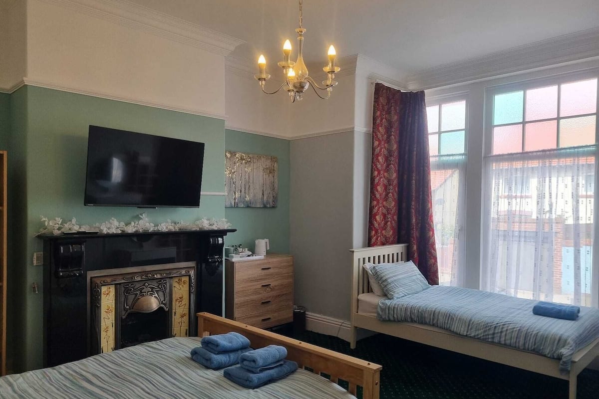 A bedroom with a fireplace, a television, a bed, and a window with curtains.