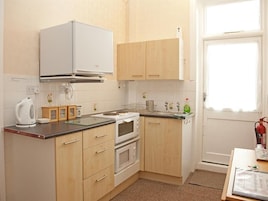 A compact kitchen with wooden cabinets, a microwave, an oven, and a window providing natural light.