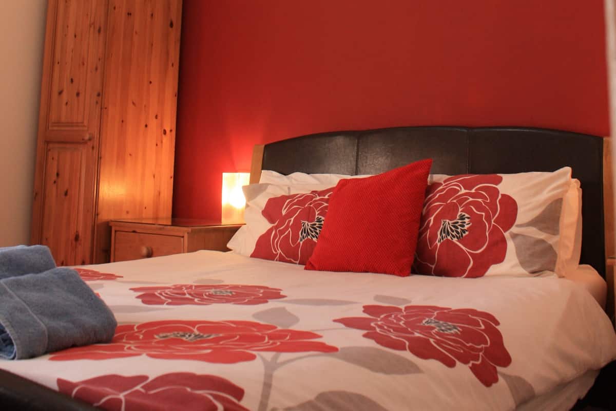 A bedroom with a bed, wooden wardrobe, and a nightstand with a lamp.