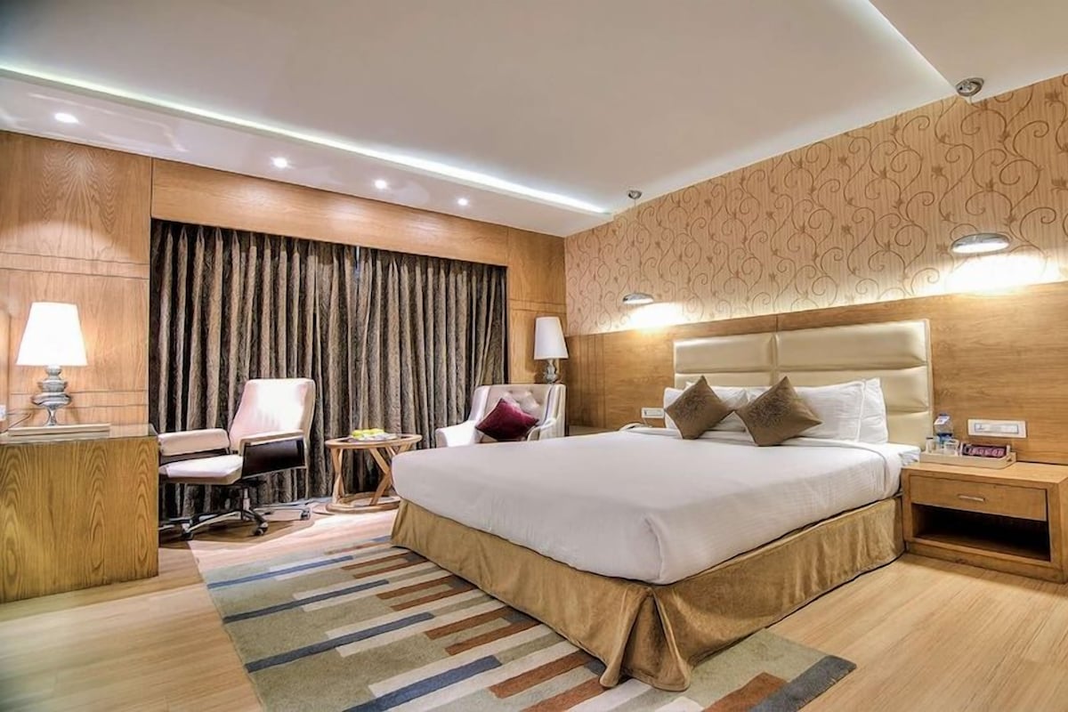 A hotel room with a large bed, a desk, a chair, a nightstand, and a patterned wall.