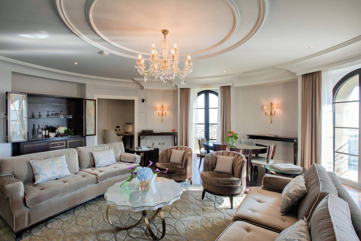 A spacious living room with a chandelier, a sofa, armchairs, and a dining area with a table and chairs.
