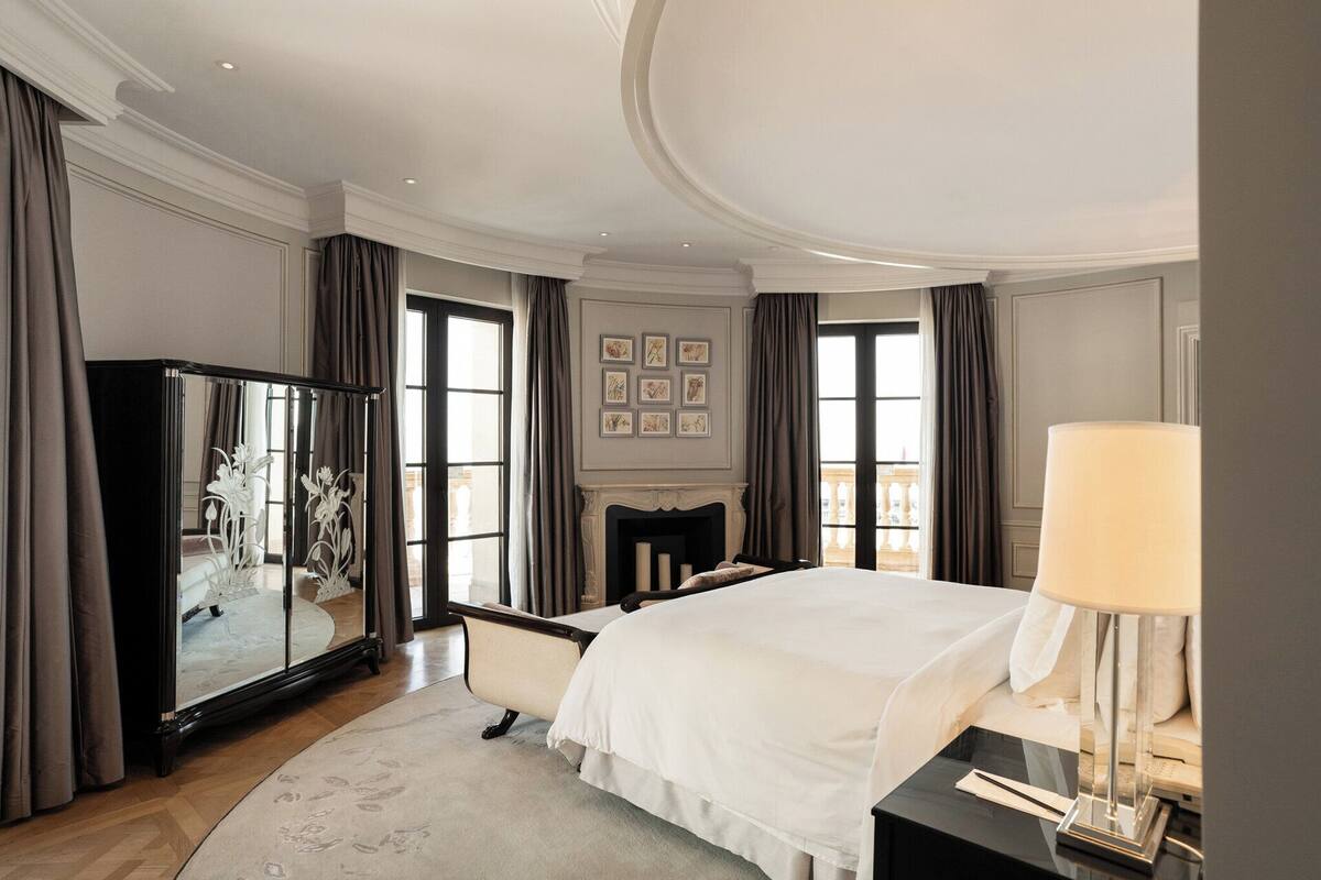 A spacious hotel bedroom with a large bed, a mirror cabinet, and a fireplace.