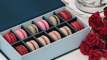 Una caja de macarons con tapa celeste, sobre una superficie blanca junto a un candelabro plateado y rosas rojas.