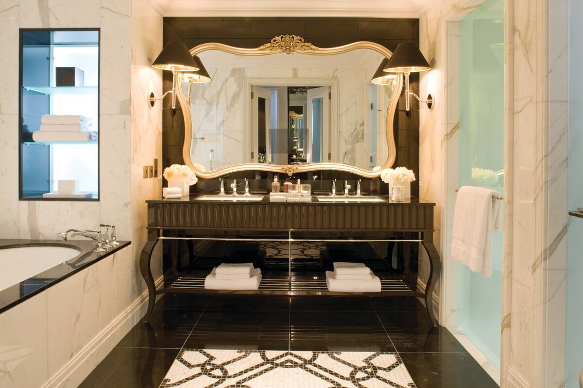 A luxurious bathroom with a large mirror, black vanity, marble floor, and a bathtub.