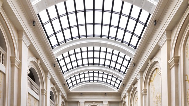 A large indoor swimming pool with a high, arched glass ceiling and classical architecture.