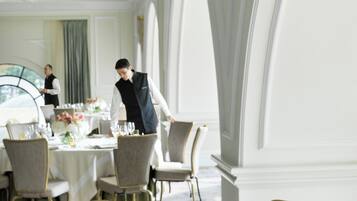 A formal dining room with tables set for service, elegant chairs, and a large floral centerpiece.