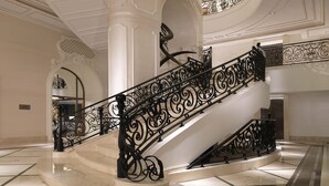 Una imponente escalera con barandillas negras ornamentadas, columnas blancas y un suelo de mármol pulido.