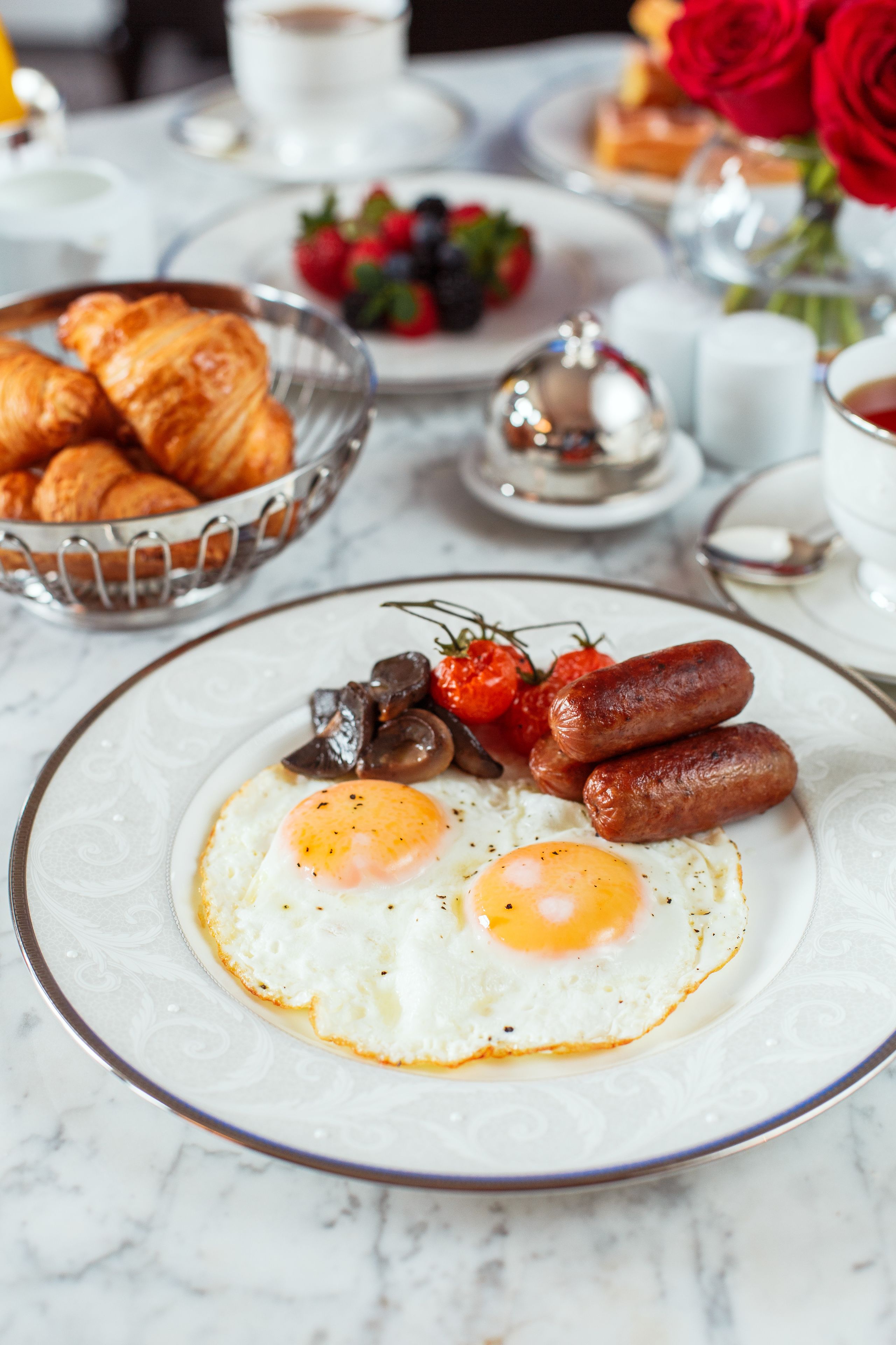 Una mesa de mármol con huevos, salchichas y una variedad de frutas y productos de pastelería para el desayuno.