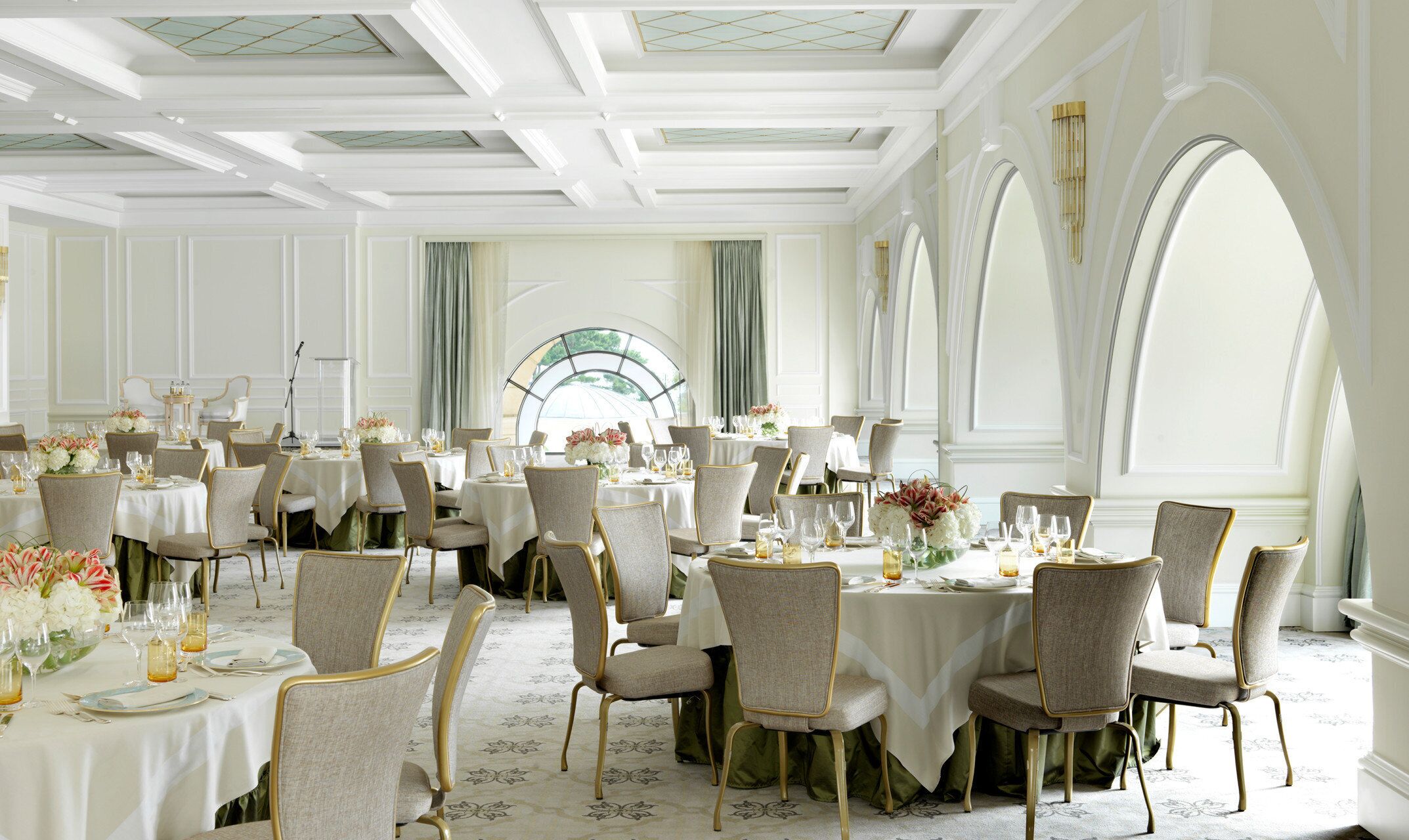 Un comedor formal con varias mesas redondas, cada una con sillas y ajuares de mesa, incluyendo centros de flores.