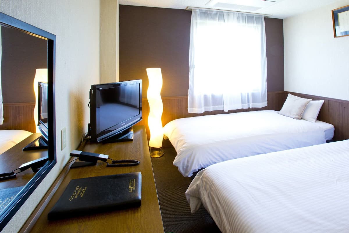 Ein Hotelzimmer mit einem Bett, einem Schreibtisch mit Fernseher, einem Telefon und einer Lampe.