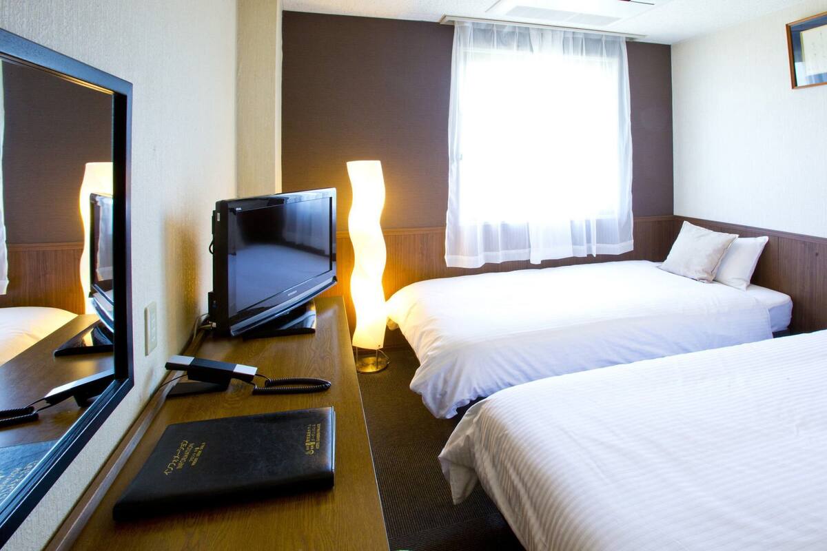 A hotel room with a bed, a desk with a television, a telephone, and a lamp.