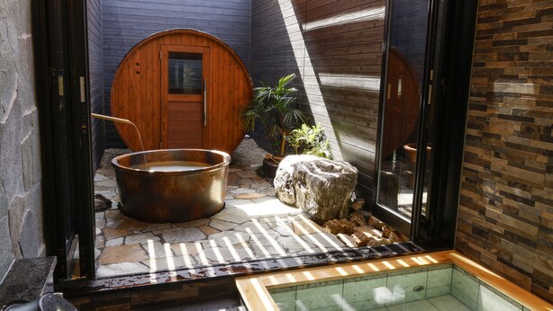 Un espace bien-être comprenant un jacuzzi, un sol en pierre, des murs en bois et une paroi en verre.