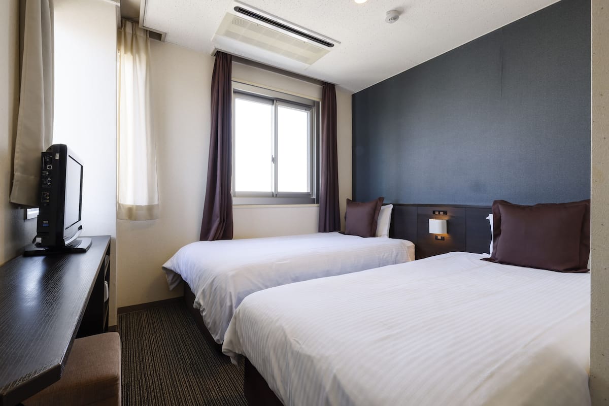 Ein Hotelzimmer mit zwei Betten, einem Schreibtisch, einem Computer und einem Fenster mit Vorhängen.
