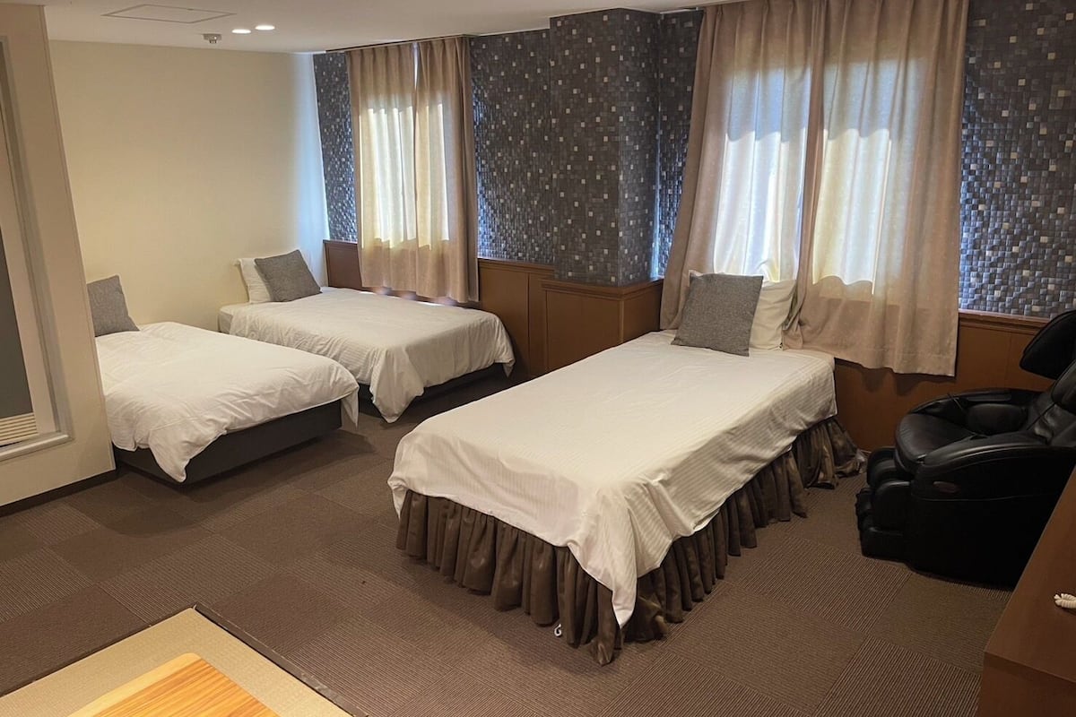 Ein Hotelzimmer mit zwei Einzelbetten, einem Massagesessel und Blick auf die Stadt.