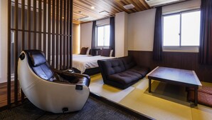 Une chambre d’hôtel moderne dotée d’un sol recouvert de tatamis, d’un canapé, d’un fauteuil massant, d’un lit et d’une petite table.