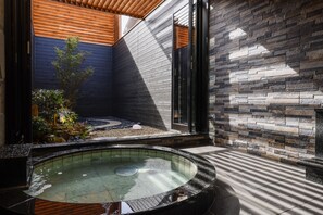 A spa area with a hot tub, wooden ceiling, stone wall, and a small garden. - Hotel Garden Palace & Kansai Airport Spa (Izumisano)