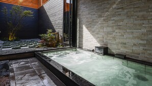 Un espace bien-être comprenant un jacuzzi, une terrasse en bois et un mur en pierre.