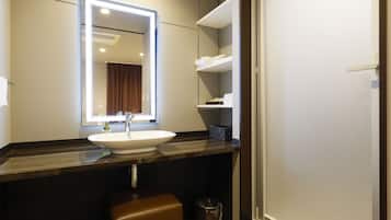 A bathroom with a large mirror, a white sink, a brown bench, and a trash can.
