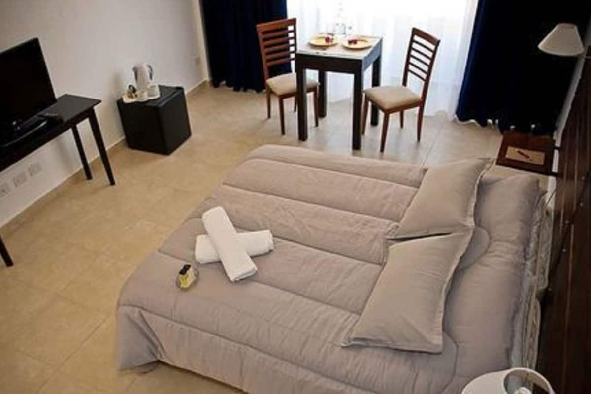 Quarto de hotel com uma cama grande, televisão, mesa pequena e duas cadeiras.