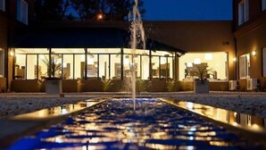 Un hotel con una fuente en primer plano, un área exterior cubierta con luces y un edificio con grandes ventanales.