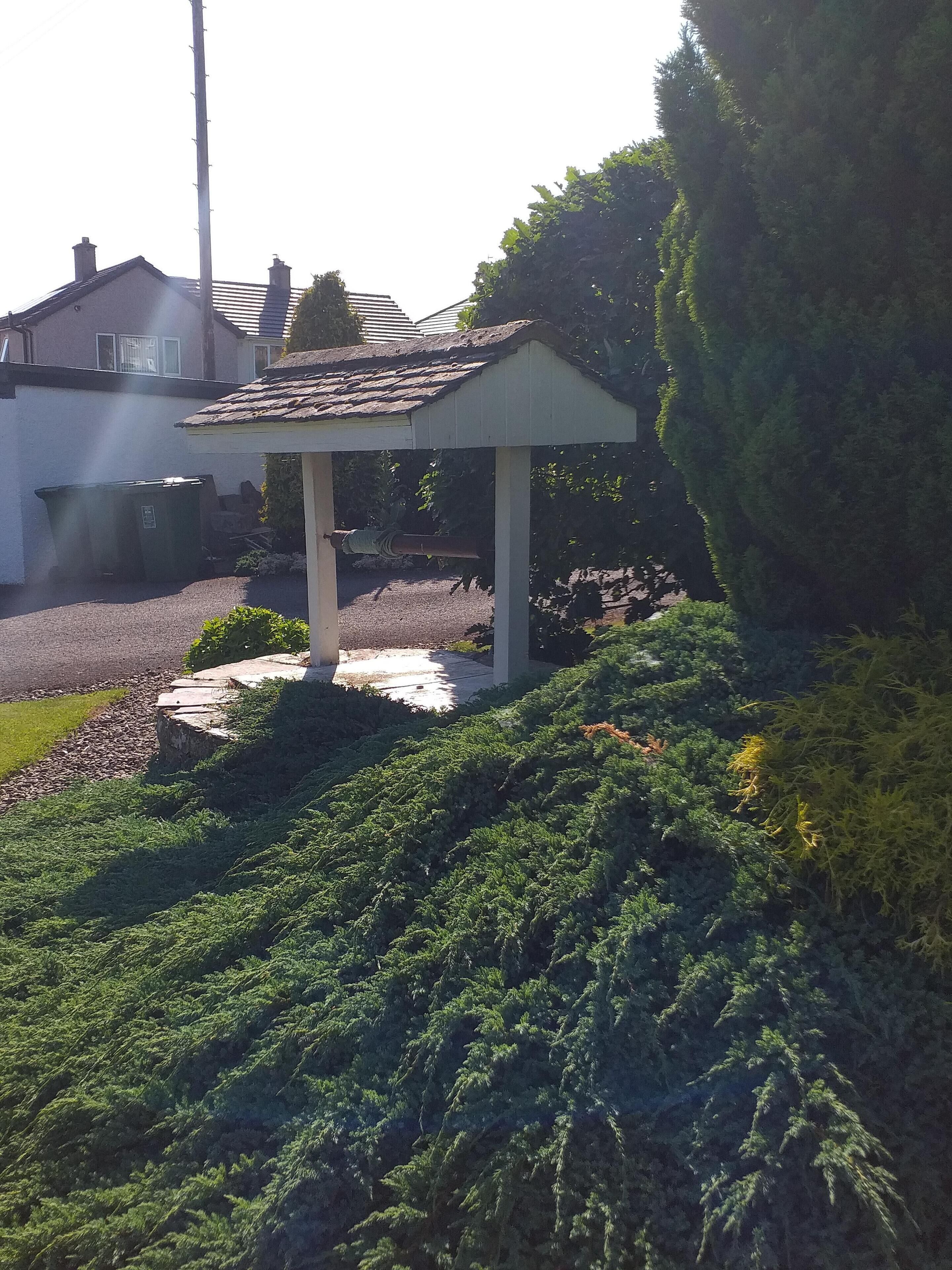 A gazebo with a tiled roof, surrounded by lush greenery and a gravel path.