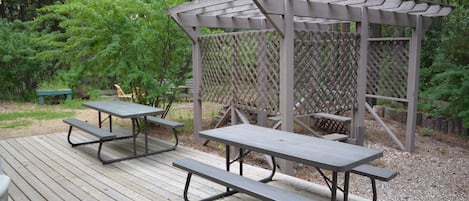 Une terrasse en bois avec des tables de pique-nique et une structure en forme de pergola.