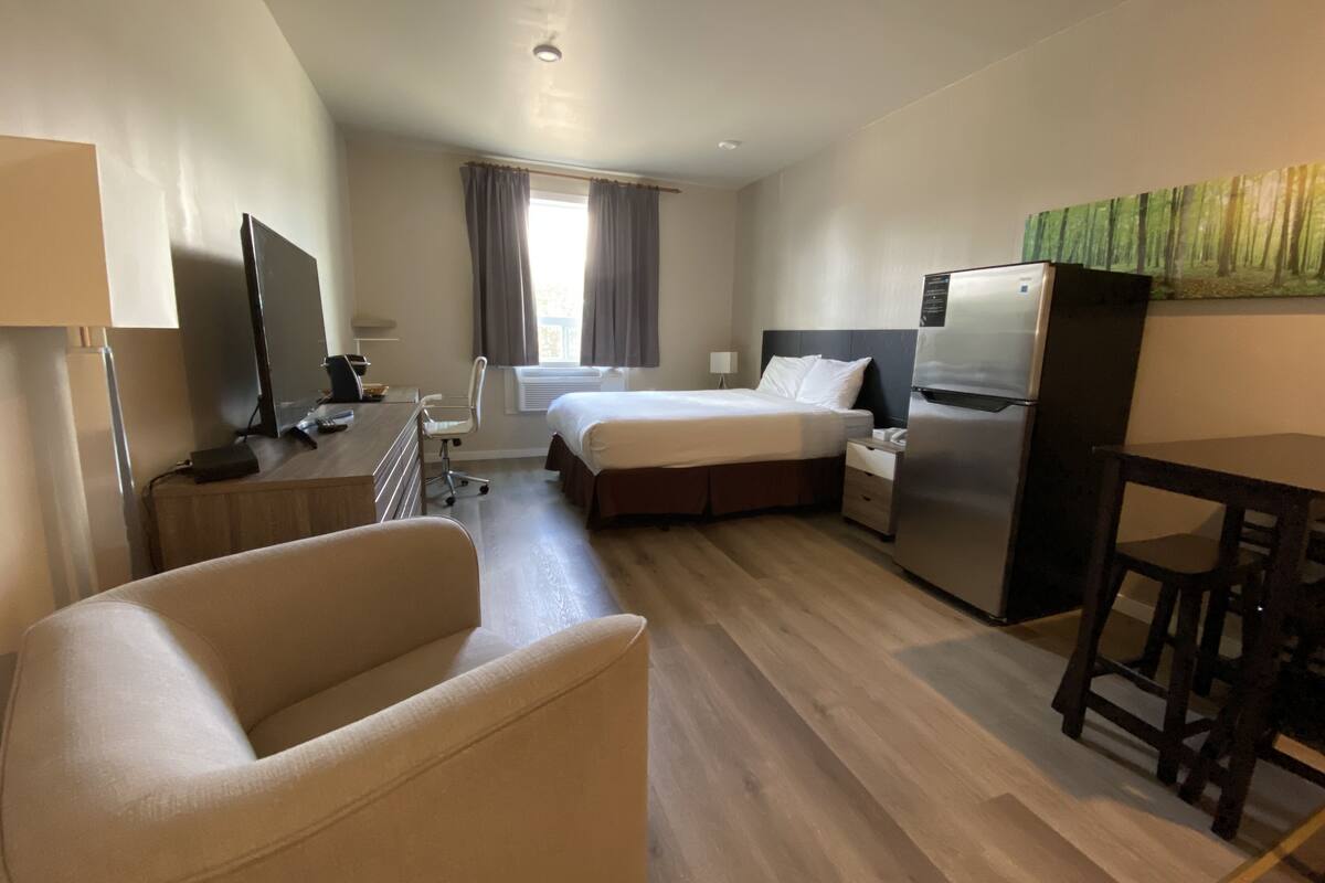 A hotel room with a bed, a desk, a chair, a TV, and a refrigerator.