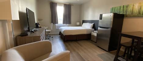 A hotel room with a bed, a desk, a chair, a TV, and a refrigerator.