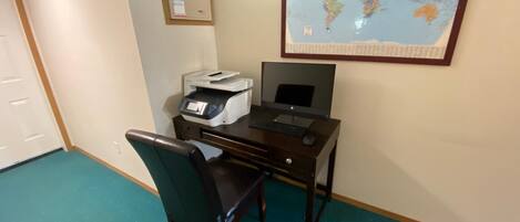 Un escritorio con una impresora y un monitor, una silla, un mapa del mundo en la pared y un detector de incendios.