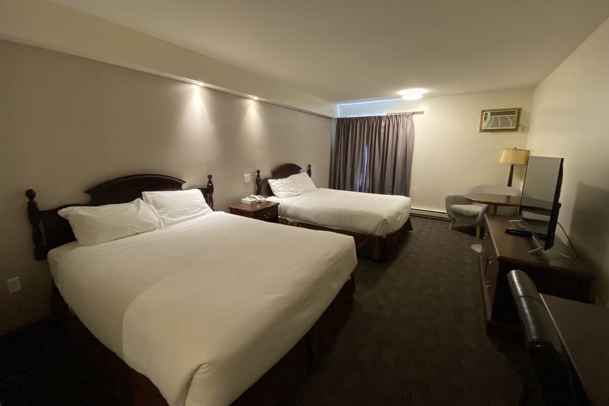 A hotel room with two beds, a desk, a chair, a lamp, and a mirror.