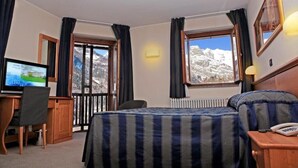 Camera d'albergo con un letto, una scrivania con un computer, una sedia, un telefono e una finestra vista montagna.