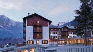 Un hotel a più piani con una facciata imponente rossa e bianca, affacciato su un corpo d'acqua con montagne sullo sfondo.