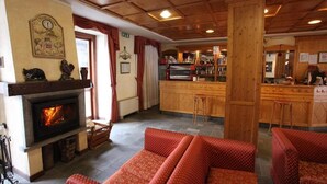 Un ambiente accogliente con camino, divani rossi a fantasia, un'area bar in legno e un pavimento in pietra.
