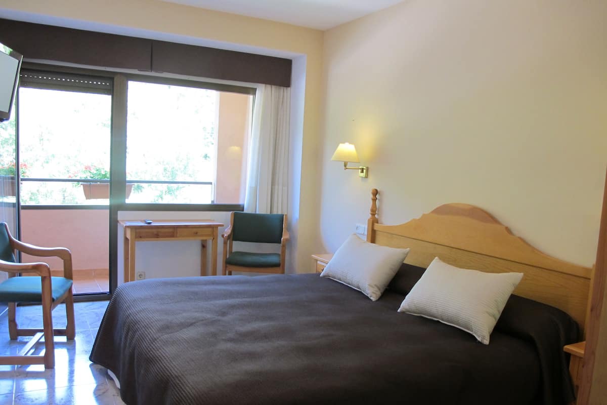 A hotel room with a bed, a desk, a chair, and a window with curtains.