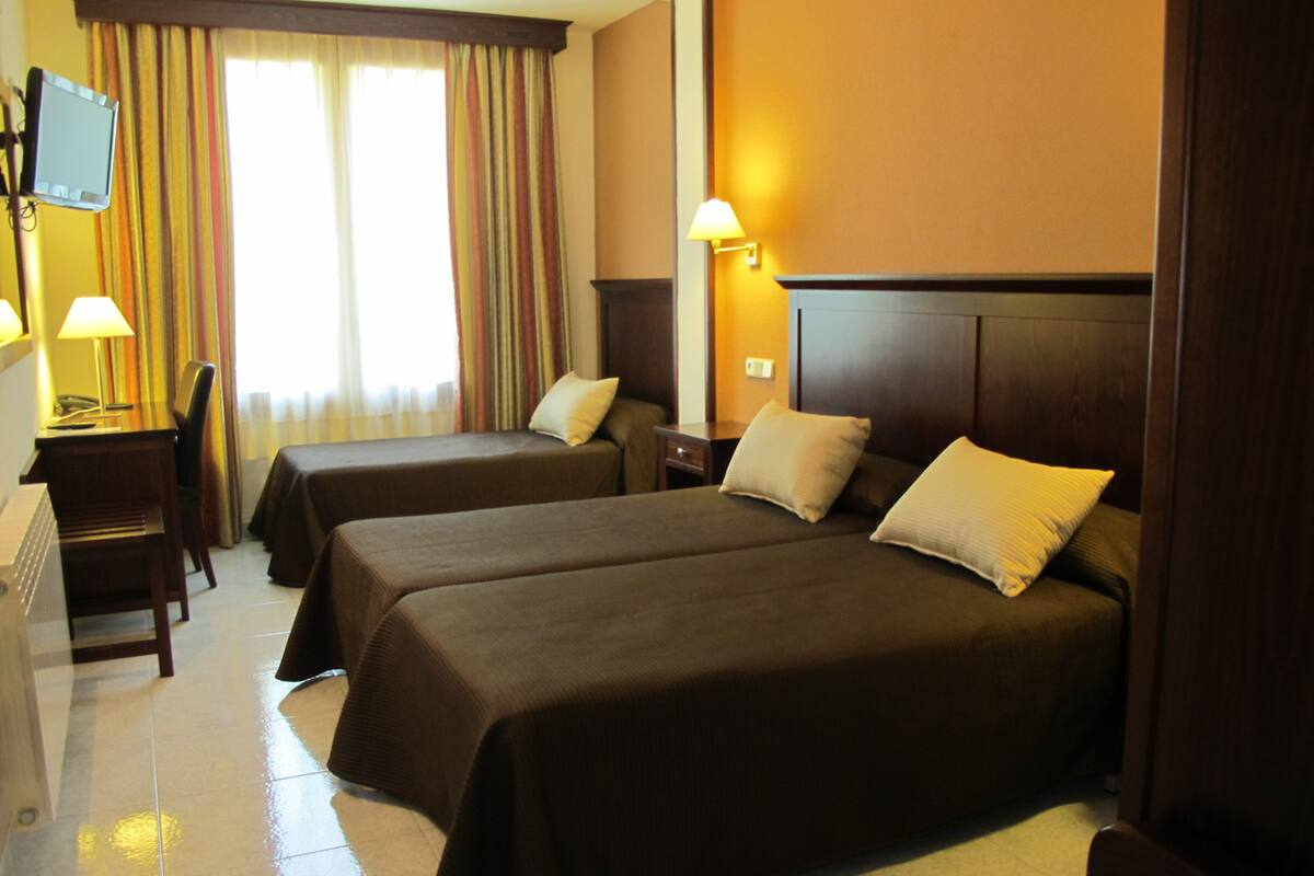 A hotel room with two beds, a desk with a lamp, a television, and a window with curtains.