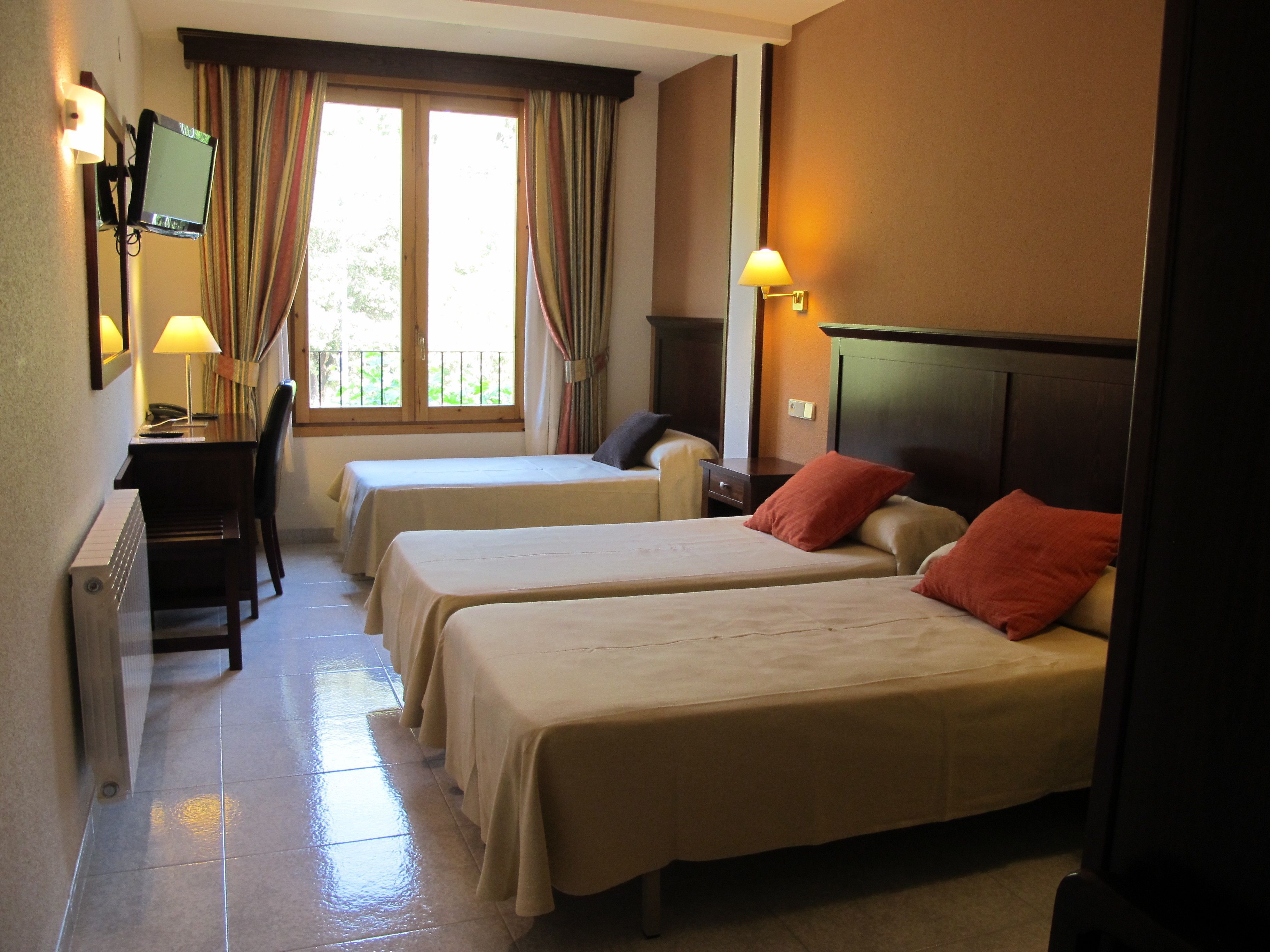 A hotel room with two beds, a desk, a chair, and a TV.