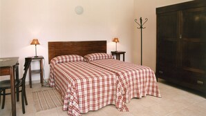 A bedroom with a bed, two bedside tables, a desk, a chair, a coat rack, and a wardrobe.