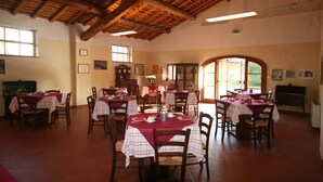 A dining area with multiple tables and chairs, wooden ceiling beams, and large windows allowing natural light.