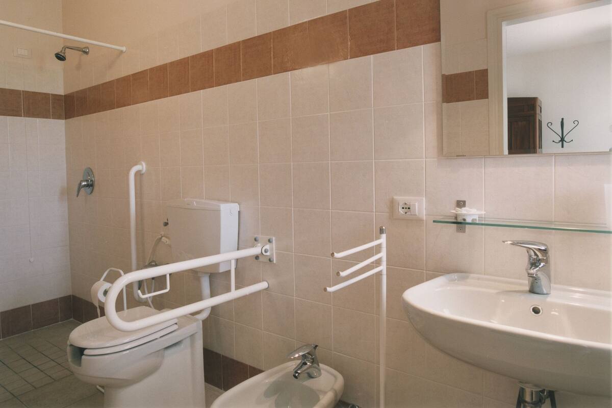 Een badkamer met toilet, bidet, wastafel en een glazen plank.