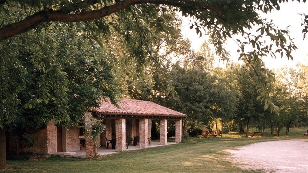 A rustic pavilion with a tiled roof, surrounded by lush greenery and trees.