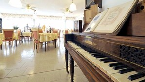 A grand piano in a spacious dining area with tables and chairs, ceiling fans, and framed certificates on the wall. - Hotel Ristorante ai Campi Di Marcello (Monfalcone)