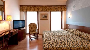 A hotel room with a bed, a desk with a television, a chair, and a window with a view. - Hotel Ristorante ai Campi Di Marcello (Monfalcone)