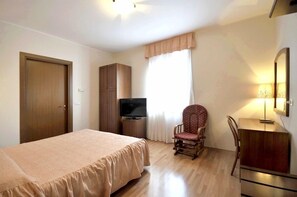 Ein Schlafzimmer mit einem Bett, einem Fernseher, einem Sessel, einem Schreibtisch und einem Kleiderschrank.